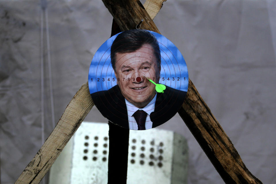 A portrait of Ukraine's embattled president Viktor Yanukovych is used for a game of darts at Independence Square in Kiev, Ukraine, Monday, Feb. 24, 2014. Ukraine’s acting government issued an arrest warrant Monday for Yanukovych, accusing him of mass crimes against the protesters who stood up for months against his rule. (AP Photo/ Marko Drobnjakovic)