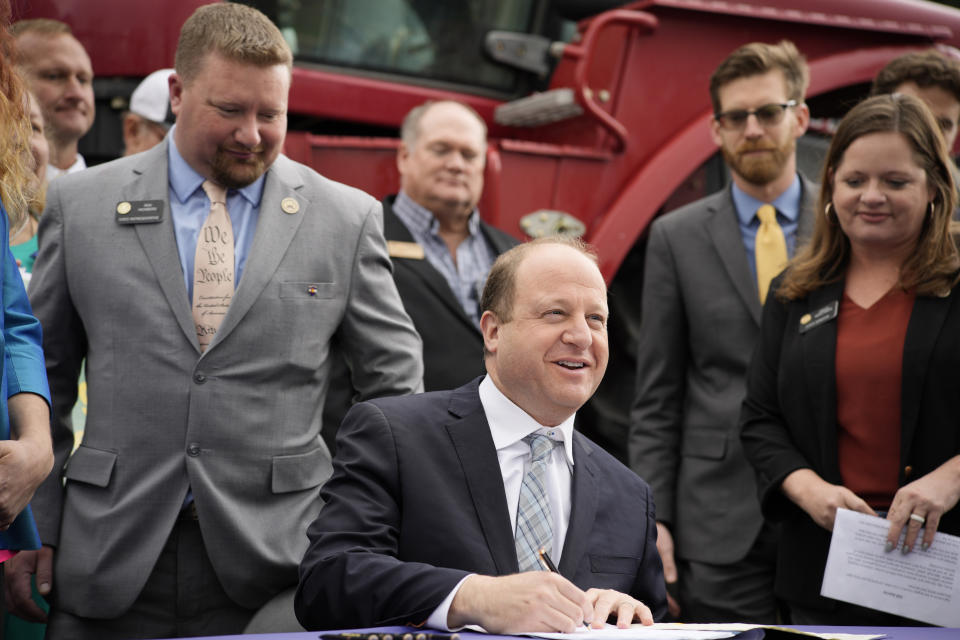 Colorado Gov. Jared Polis signs legislation that forces manufacturers to provide the necessary manuals, tools, parts and even software to farmers so they can fix their own machines Tuesday, April 25, 2023, during a ceremony outside the State Capitol in downtown Denver. Colorado is the first state to put the right-to-repair law into effect while at least 10 other states are considering similar measures. Looking on are Rep. Ron Weinberg, back left, and Sen. Janice Marchman. (AP Photo/David Zalubowski)