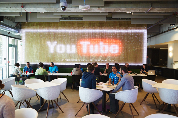 Google employees eating at the company's YouTube cafe with a large YouTube Logo in the background