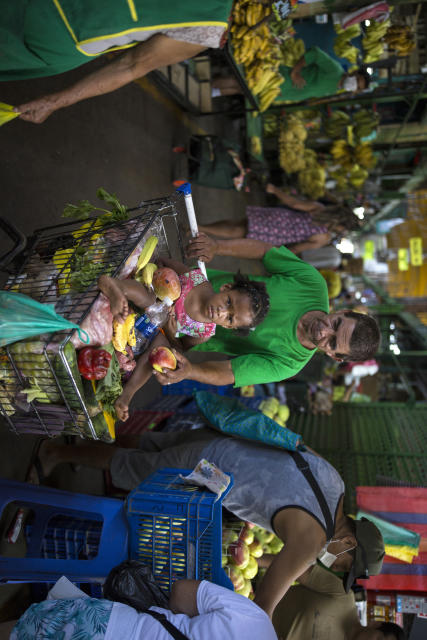 In this March 18, 2020 photo, Cesar Alegre, accompanied by his 4-year-old daughter Lia, places a damaged apple in his shopping cart filled with discarded produce given to him by vendors at a popular market in Lima, Peru. It is a task that was hard at the best of times, but with a month-long quarantine to curb the spread of the new coronavirus that has forced millions of Peruvians to stay home and closed restaurants and food kitchens, it has become much harder to feed his children. “The virus has highlighted the selfishness that man carries inside,” said Alegre. (AP Photo/Rodrigo Abd)