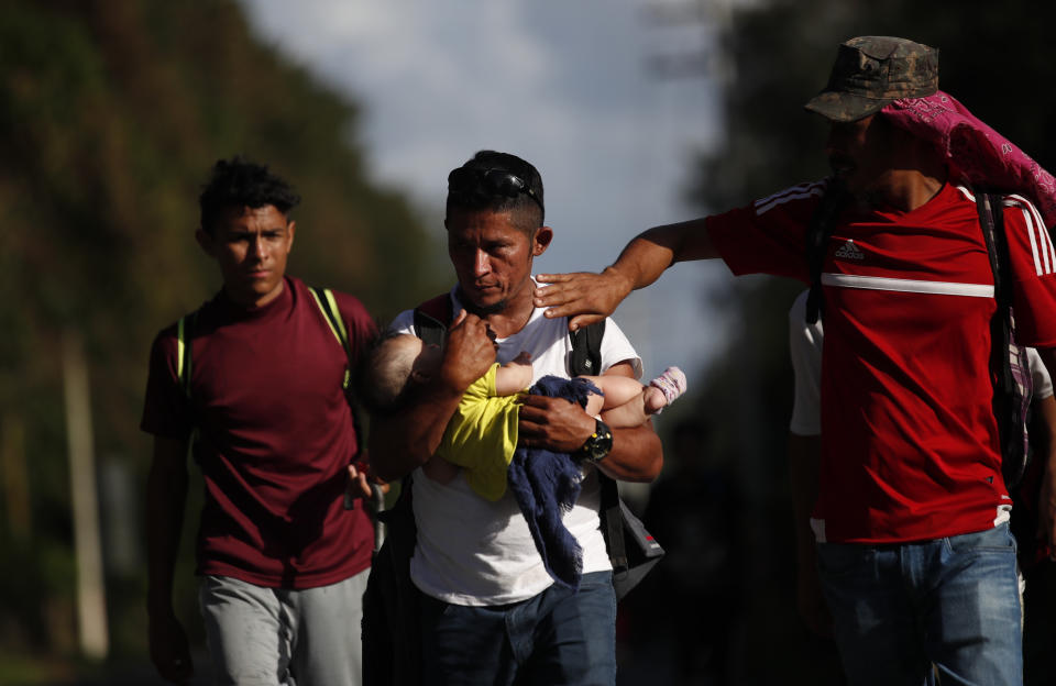 Honduran migrant Selvin Hernandez carries Mayra Irene, the baby daughter of another migrant, as another man tries to shade her with his hand amid a group of migrants trying to make it to the United States, near El Cinchado, Guatemala, Wednesday, Jan. 15, 2020, on the border with Honduras. (AP Photo/Moises Castillo)