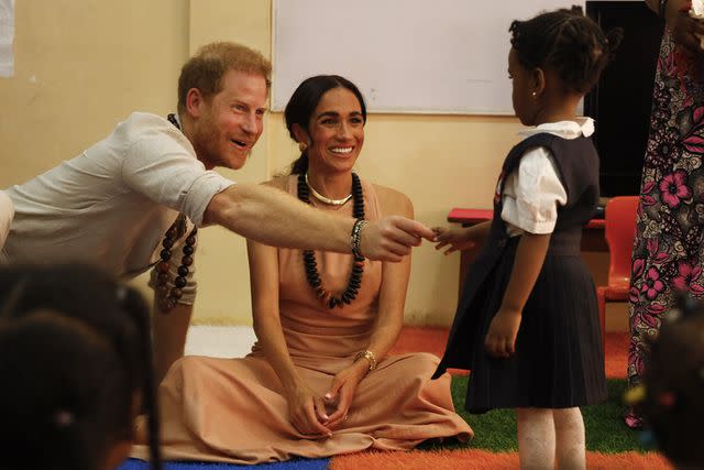 <p>Andrew Esiebo/Getty</p> Prince Harry (Left) and Meghan Markle greet a student in Nigeria