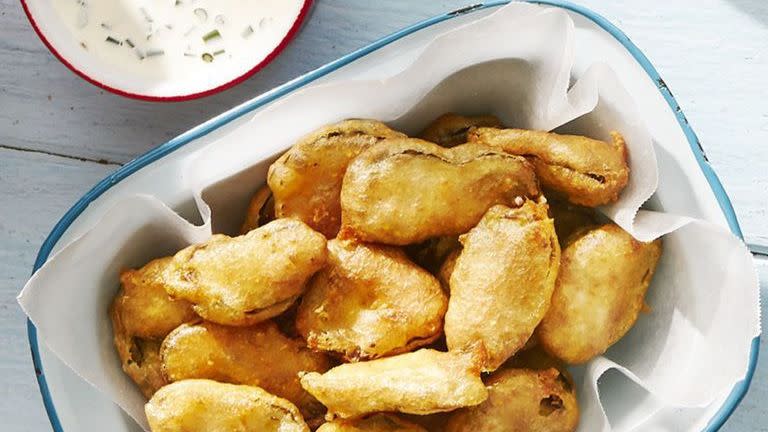 fried pickles in a parchment paper lined serving dish on a white wooden table outside with a small bowl of ranch for dipping