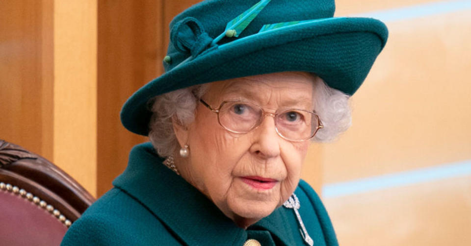 Queen Elizabeth II wearing a green outfit and green hat, and glasses.