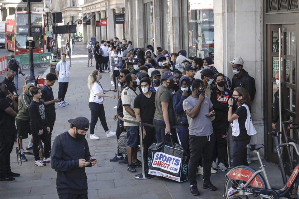 Nike employees speak to people queueing outside the Niketown shop attempting to get them to maintain social distancing in London, Monday, June 15, 2020. After three months of being closed under coronavirus restrictions, shops selling fashion, toys and other non-essential goods are being allowed to reopen across England for the first time since the country went into lockdown in March.(AP Photo/Matt Dunham)