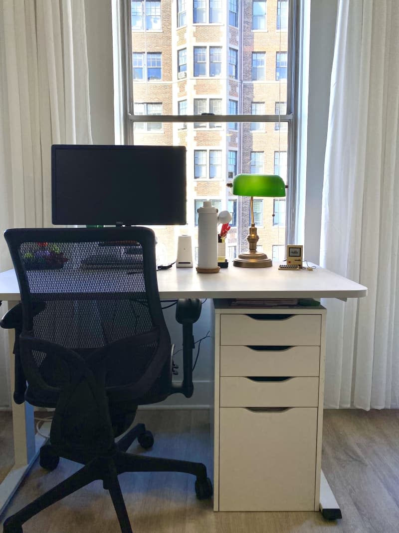 Black desk chair at a white desk with a computer monitor and green lamp.