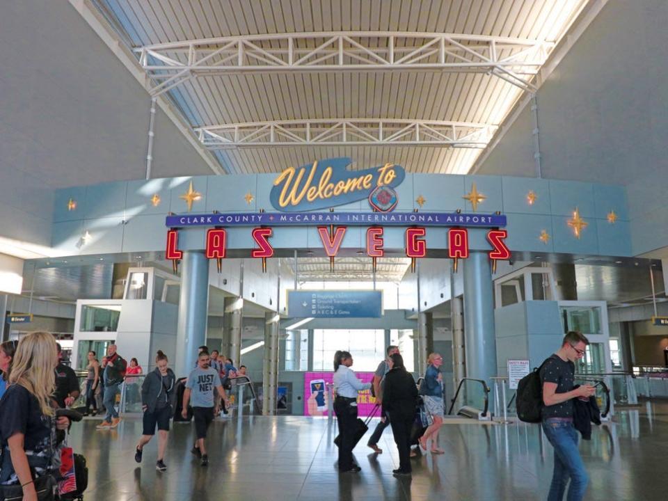 Passengers with backpacks and luggage walking under an arch at Harry Reid International Airport.