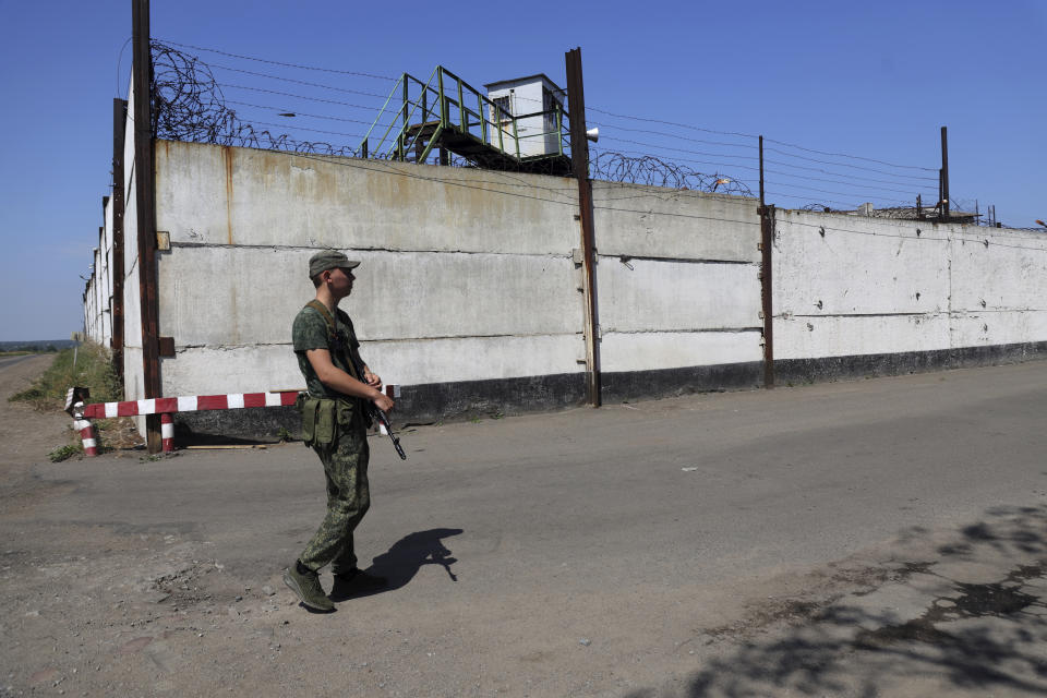 A soldier stand guard next to a wall of a prison in Olenivka, in an area controlled by Russian-backed separatist forces, eastern Ukraine, Friday, July 29, 2022. Russia and Ukraine accused each other Friday of shelling a prison in a separatist region of eastern Ukraine, an attack that reportedly killed dozens of Ukrainian military prisoners who were captured after the fall of a southern port city of Mariupol in May. (AP Photo)