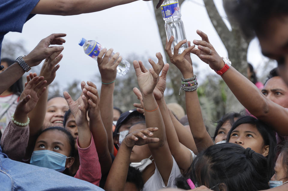 Residents scramble to grab bottled water given by a passing citizen at a town near Taal volcano, Tagaytay, Cavite province, southern Philippines on Sunday Jan.19, 2020. Many poor families living near Taal volcano have been affected due to loss of income after business closures in the area, Philippine officials said Sunday the government will no longer allow villagers to return to a crater-studded island where an erupting Taal volcano lies, warning that living there would be "like having a gun pointed at you." (AP Photo/Aaron Favila)