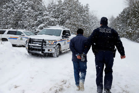 FILE PHOTO: A man who told police that he was from Sudan is taken into custody by a Royal Canadian Mounted Police (RCMP) officer after arriving by taxi and walking across the U.S.-Canada border into Hemmingford, Quebec, Canada on February 13, 2017. REUTERS/Christinne Muschi/File Photo