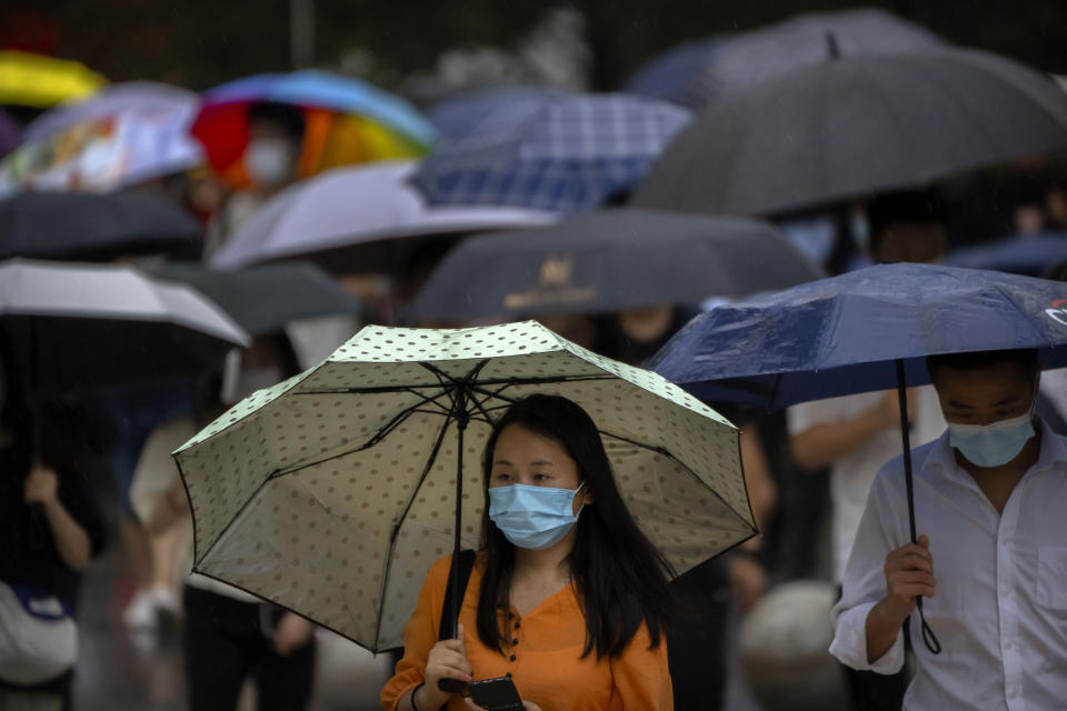 A woman wearing a face mask carries an umbrella as she walks along a street in the central business district in Beijing, Tuesday, Aug. 9, 2022. Chinese authorities have closed Tibet's famed Potala Palace after a minor outbreak of COVID-19 was reported in the Himalayan region. (AP Photo/Mark Schiefelbein)