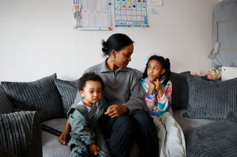A woman sitting on a sofa with her arms around two young children