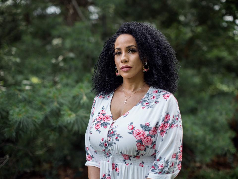 Woman in a flowered dress standing in front of some lush green trees.