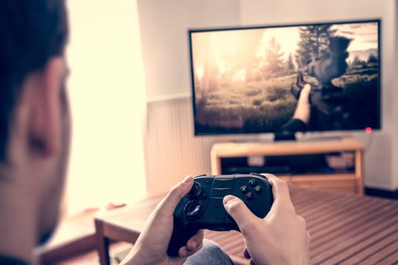 over the shoulder view of a gamer playing a first person shooter video game on a TV screen.