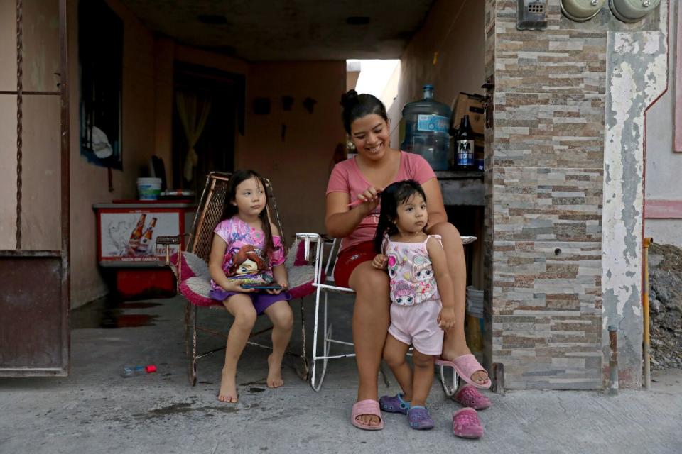 A woman brushes a young girl's hair as another girl watches