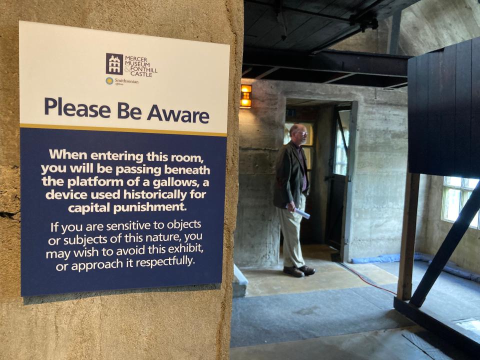 Warning sign at the Mercer Museum posted at the entrance of a passageway that contains a gallows used to hang convicted criminals. "People don't even realize what they're passing under, so we have the sign to warn them. Some people are sensitive to things like this," said Cory Amsler (standing), vice president of collections and interpretation at the Mercer Museum in Doylestown.