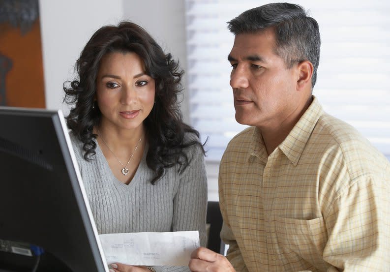 Couple holding a document and looking at a computer screen together.