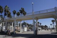 A man bikes under a bridge connecting the Oceanside pier to Pacific Street Friday, Oct. 15, 2021, in Oceanside, Calif. The iconic bridge is deteriorating because the city lacks the money for a roughly $25 million rehabilitation. One reason the project has slowed while projects in other cities are moving ahead revolves around the American Rescue Plan — the sweeping COVID-19 relief law championed by President Joe Biden and congressional Democrats that is pumping billions of dollars to states and local governments. (AP Photo/Gregory Bull)