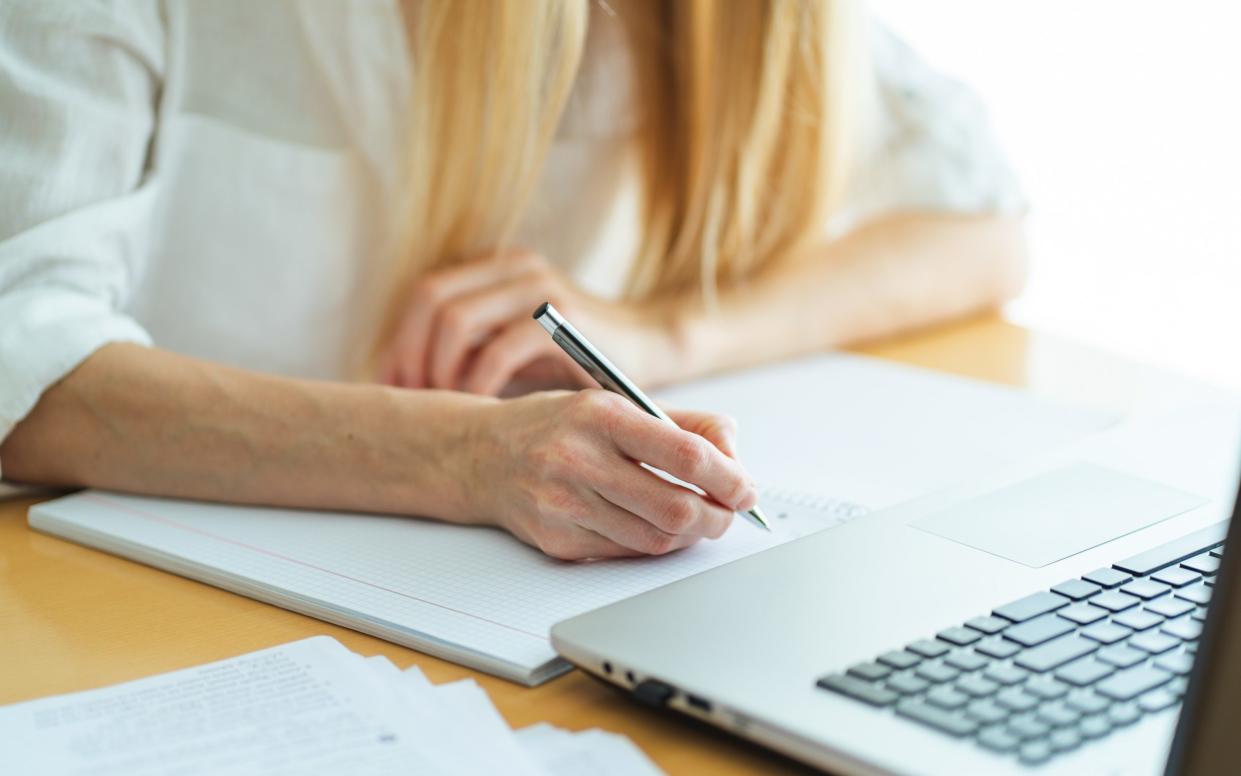 Close up of woman hands writing in textbook near laptop.