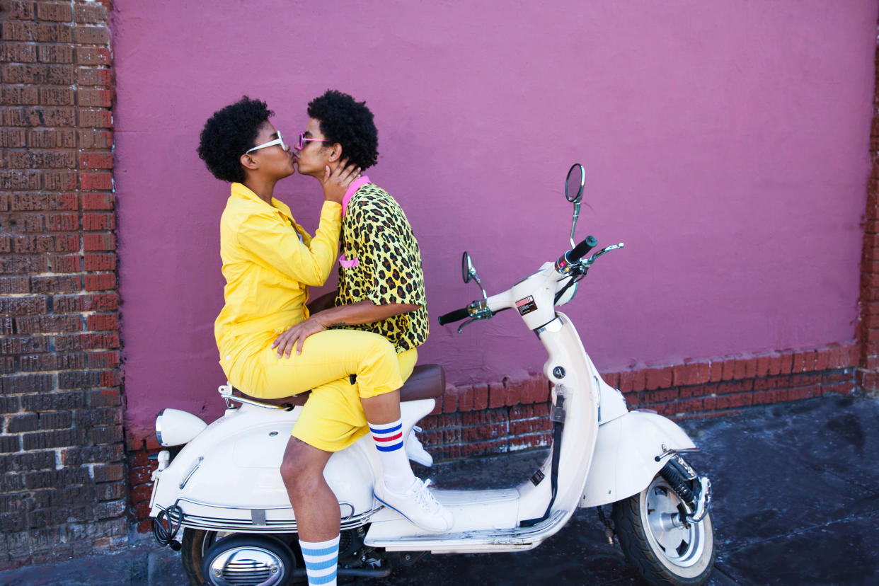 A young couple wearing yellow outfits sitting on a scooter kissing