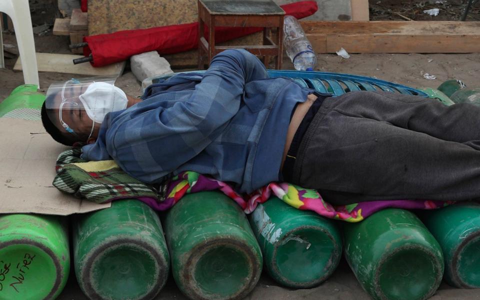 A man sleeps on top of empty oxygen cylinders - AP