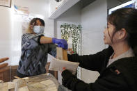 Server Lieda Hay, left, hands a take-out order to customer Molly Ha at Chung Chun Rice Dog restaurant in the Chinatown-International District, Monday, March 16, 2020, in Seattle. Washington Gov. Jay Inslee on Monday ordered all bars, restaurants, entertainment and recreation facilities to temporarily close to fight the spread of the new coronavirus in the state with by far the most deaths in the U.S. from the COVID-19 disease. Take out and delivery food orders are still allowed. (AP Photo/Elaine Thompson)