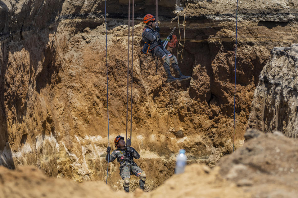 Rescuers from the Guatemalan Army descend into a sinkhole in Villa Nueva, Guatemala, Tuesday, Sept. 27, 2022. Search efforts continue for a mother and daughter who disappeared when their vehicle was swallowed by the massive sinkhole. (AP Photo/Moises Castillo)