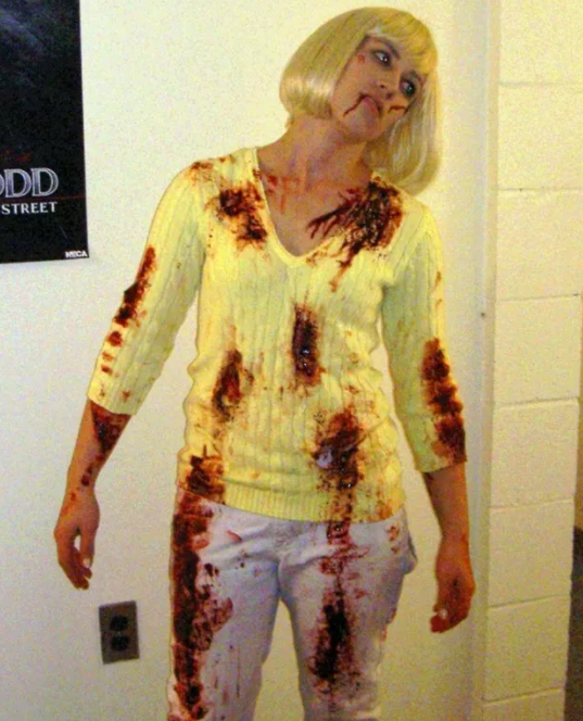 Woman in platinum wig with "blood" spattered on her sweater and pants