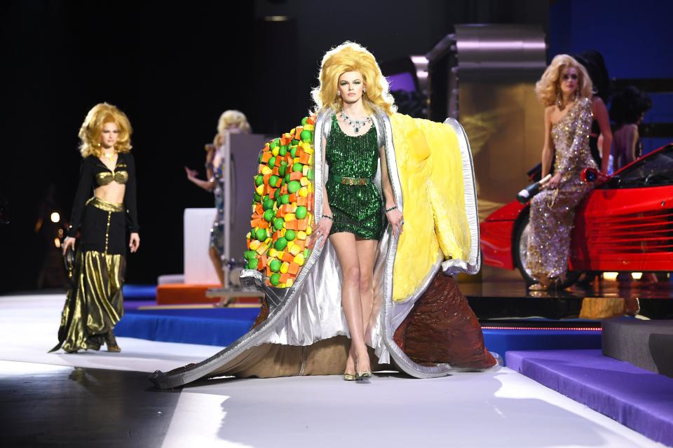 <p>Jeremy Scott's Moschino shows are always high on camp and stick to a clear theme. This season, as soon show goers heard the first few notes from the <a rel="nofollow noopener" href="https://www.youtube.com/watch?v=13tnjh3dZw4" target="_blank" data-ylk="slk:musical accompaniment we knew what to expect;elm:context_link;itc:0;sec:content-canvas" class="link ">musical accompaniment we knew what to expect</a>: A fully functional <em>Price is Right</em> set complete with glimmering lights, a Ferrari on a spinning platform, and models like Kaia Gerber, Jasmine Sanders, and Bella Hadid glammed up like retro <a rel="nofollow noopener" href="http://www.thoughtrot.com/the-price-is-right-the-original-barkers-beauties/" target="_blank" data-ylk="slk:Barker’s Beauties;elm:context_link;itc:0;sec:content-canvas" class="link ">Barker’s Beauties</a>. Moschino’s fall collection was an ode to the game show (and others like <em>Wheel of Fortune</em> and <em>Press Your Luck</em>), but juiced up to the next level. </p><p>Always down for a good time, Scott showed blinged out gowns, dresses that lit up, and even a TV dinner kimono. These aren't pieces you would wear straight off the runway, but they do bring a sense of levity many of us are so desperate for these days. But if you are looking for pieces you could try in your everyday life, the dollar sign gear, fur coats, and cocktail dresses will do the trick. </p>