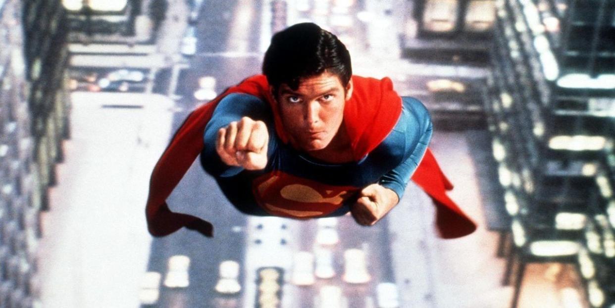 actor christopher reeve as superman flying through the air in his iconic blue and red superhero costume with a red cape
