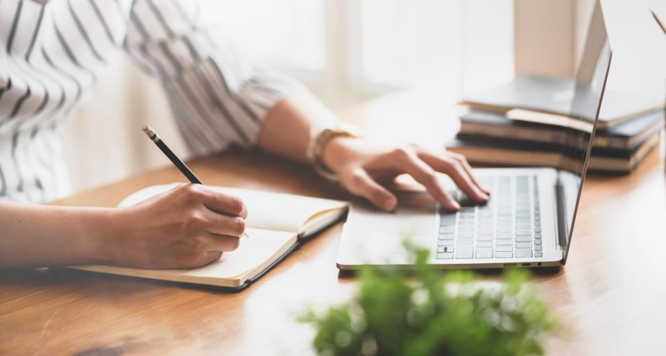 woman writing notes in notebook looking at laptop