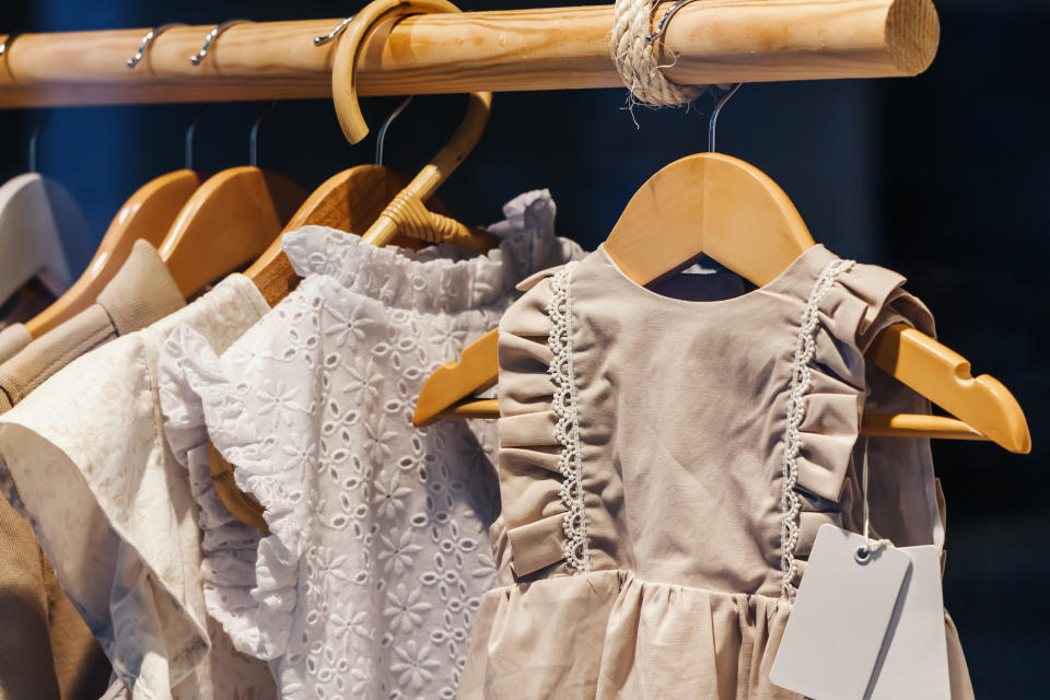 Children's clothes, including a frilly dress with lace trim, hang on a wooden rack