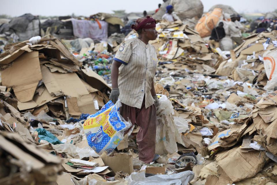 In this photo taken Friday, Jan, 24. 2014, a scavenger in Lagos, Nigeria sorts out iron and plastic to sell at the Olusosun dump site the city's largest dump. With a population of more than 20 million, garbage piles up on streets, outside homes and along the waterways and lagoons, creating eyesores and putrid smells. The booming city also has major electricity shortages and many residents rely on diesel generators that cloud the air with black exhaust. Nigeria's most populous city is turning these problems into an advantage by starting a program to convert waste into methane gas to generate electricity. A pilot program at a local market has already shown success on a smaller scale. Lagos’ waste management program is also organizing recycling to clean up the country's biggest city. (AP Photo/ Sunday Alamba)