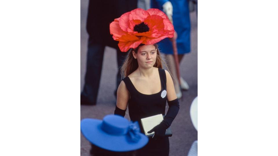 A female racegoer wearing a black dress, black evening gloves, and a red poppy hat on the first day of the Royal Ascot, 19 June 1990.