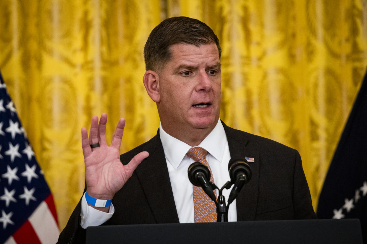Marty Walsh speaks into two microphones at a podium in front of a yellow curtain next to an American flag.