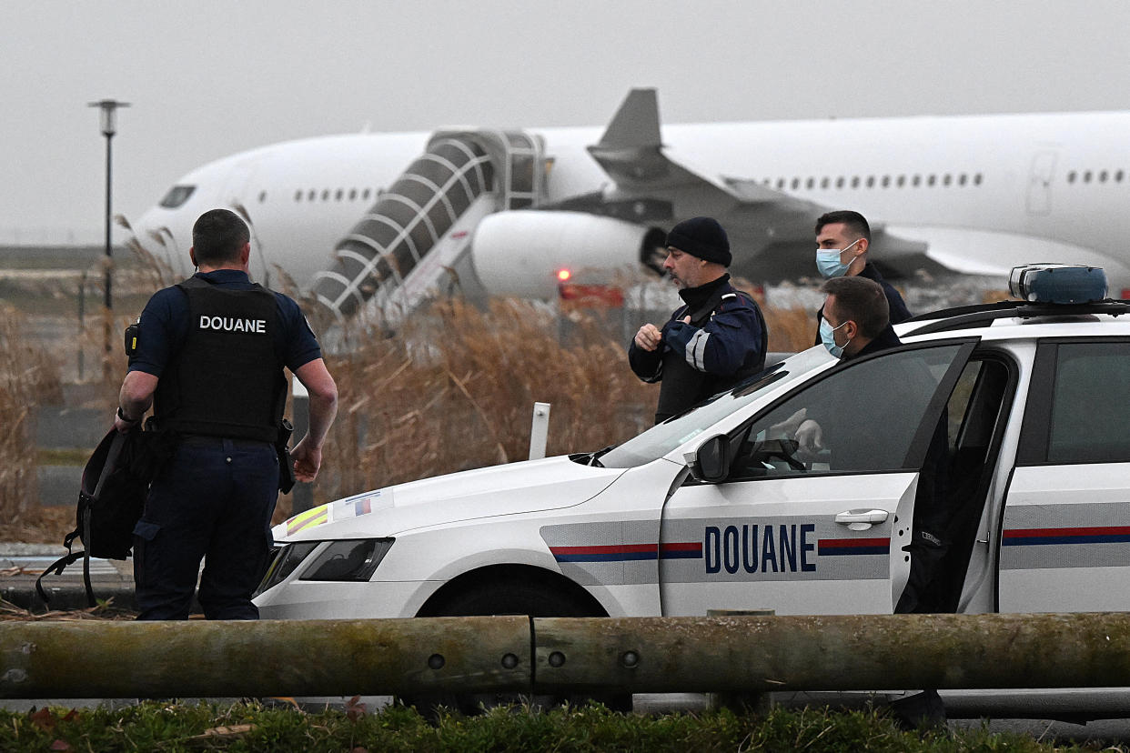 French customs officers stand next to a customs car with an Airbus A340 in the background which was grounded on the tarmac since December 21 over suspected "human trafficking", at the Vatry airport, north-eastern France on December 25, 2023. Two Indians passengers on the flight grounded since December 21, in the Marne region of France on suspicion of human trafficking will be presented to an examining magistrate on December 25, with possible indictment, while most of the other passengers are due to take off for India later on December 25. (Photo by FRANCOIS NASCIMBENI / AFP)