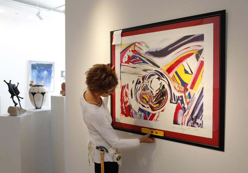 This photo taken Aug. 21, 2013, shows Betsy Orbe Lester hanging a color lithograph by James Rosenquist at the Morean Arts Center in St. Petersburg, Fla. Rosenquist, a key figure in the pop art movement, has died. He was 83. Rosenquist’s wife, Mimi Thompson, told The New York Times that he died Friday, March 31, 2017, in New York City after a long illness. ( James Borchuck/Tampa Bay Times via AP)