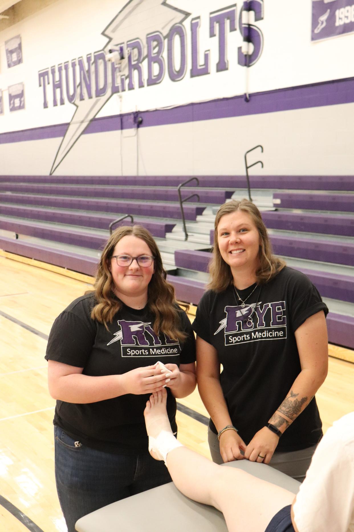 Recent Rye High School graduate Amelia Burbidge (left) and sports medicine instructor Kortney Sorensen tape up a student's ankle in the Rye High School gymnasium.