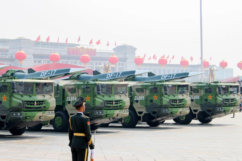 A Chinese soldier stands at attention during a military parade, as trucks display hypersonic missiles in the backgorund.