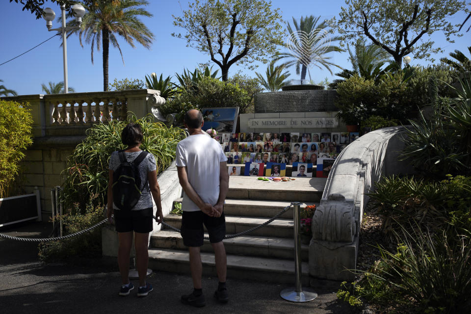Onlookers pay respect on the memorial of the victims of the attack of July 14, 2016 with pictures of the victims and "In Memory of our Angels" engraved on the wall along Nice's Promenade des Anglais, to commemorate the 2016 terror attack, in Nice, South of France, Sunday, Sept. 4, 2022. Eight suspects will face trial in a Paris Court on Monday, in connection with the 2016 Bastille Day truck attack in Nice that left 86 people dead. (AP Photo/Daniel Cole)
