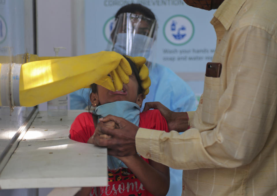 An adult helps hold a child as his nasal swab sample is taken by a health worker at a COVID-19 testing center in Hyderabad, India, Saturday, Oct. 3, 2020. India has crossed 100,000 confirmed COVID-19 deaths on Saturday, putting the country's toll at nearly 10% of the global fatalities and behind only the United States and Brazil. (AP Photo/Mahesh Kumar A.)