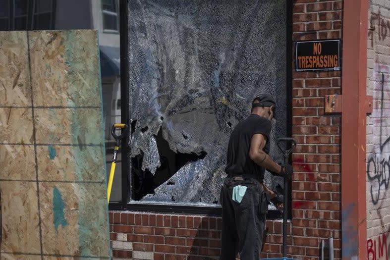 <p>A man cleans up a broken window to a barber shop after shots were fired in George Floyd Square on the one year anniversary of Mr Floyd’s death</p> (AP)