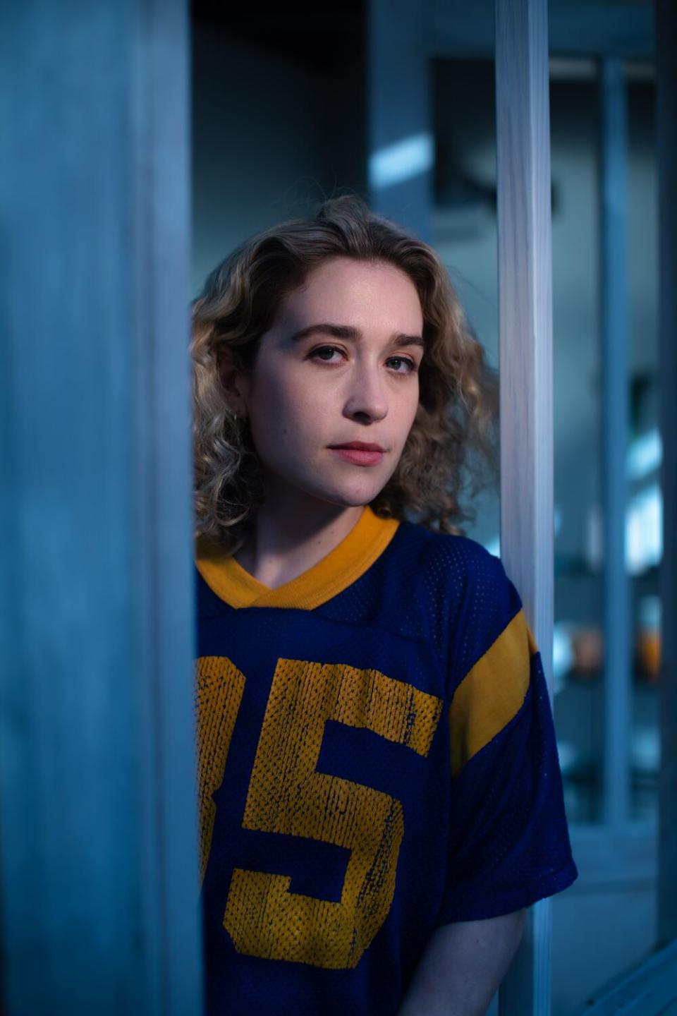 A female rock musician peers out from behind a blue wall