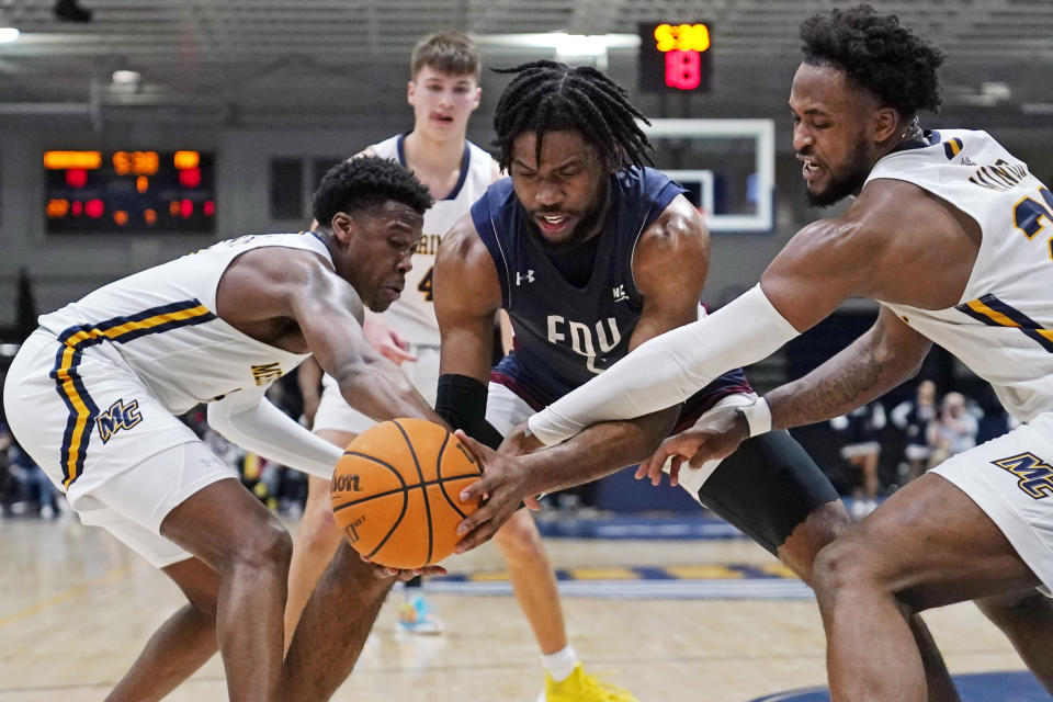 Fairleigh Dickinson forward Ansley Almonor, center, battles for the ball against Merrimack guard Devon Savage, left, and forward Jordan Minor, right, during the first half of Northeast Conference men's NCAA college basketball championship game, Tuesday, March 7, 2023, in North Andover, Mass. (AP Photo/Charles Krupa)