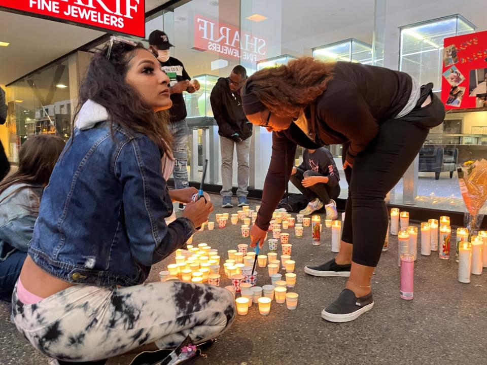 Elexus Harris, left, whose brother Sergio Harris was killed in Sunday's mass shooting, helps light candles on a sidewalk