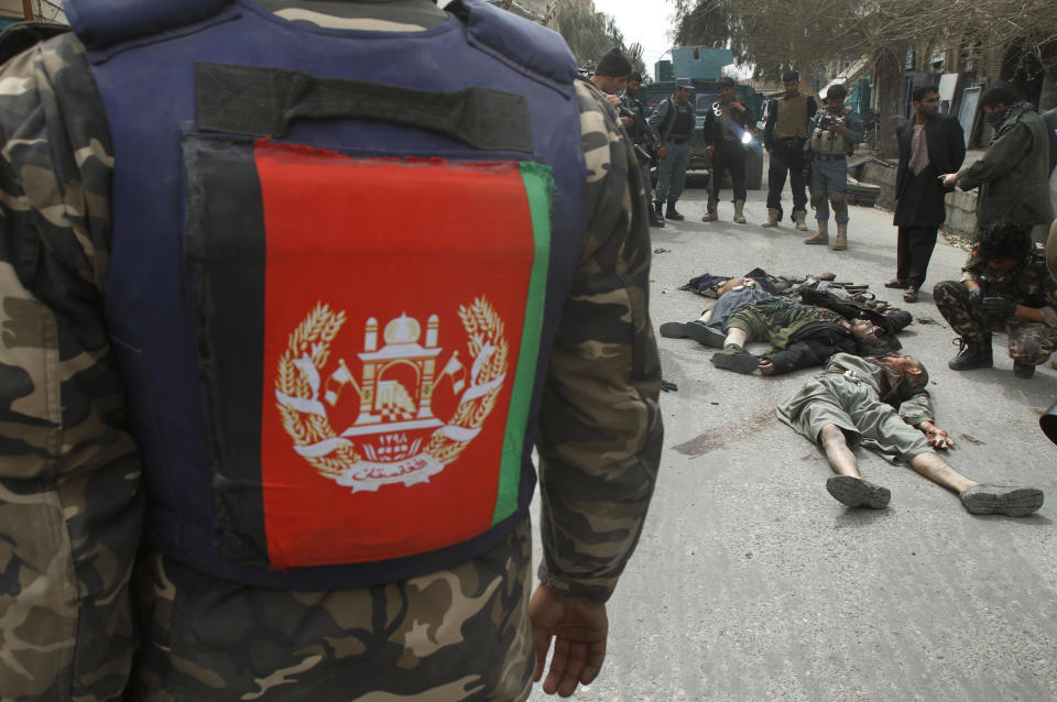 CAPTION CORRECTION, CORRECTS PHOTOGRAPHER'S NAME IN SIGNOFF - An Afghan National Intelligent officers has his bullet proof vest rapped into the Afghan flag as he inspects dead suicide fighters after an attack on the former Afghan intelligence headquarters in the center of Kandahar, Afghanistan, Wednesday, March 12, 2014. Afghan police officials said three insurgents tried to storm the former intelligence service headquarters in the southern city of Kandahar, prompting a fierce gunbattle with security forces that left the attackers dead. (AP Photo/Allauddin Khan)