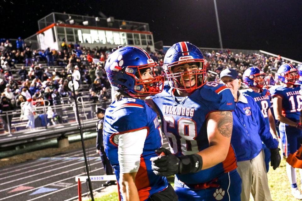 Mason's Nick Saade, right, hugs quarterback Cason Carswell on the sideline late during the fourth quarter in the game against DeWitt on Friday, Nov. 3, 2023, at Mason High School.