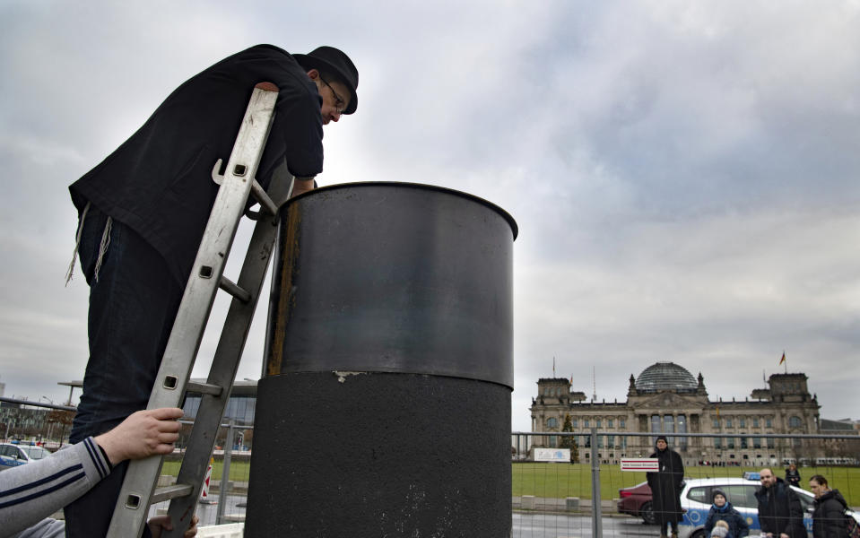 The author Eliyah Havemann reattaches a previously dismantled steel plate to the controversial steel column of the artists' collective "Centre for Political Beauty" (ZPS) opposite the Reichstag building in Berlin Germany, Sunday, Jan.5, 2019. Several activists have tried to dismantle the controversial steel column of the artists' collective "Centre for Political Beauty" (ZPS) in Berlin. "One should not make art and politics with ashes of victims of the Holocaust," Havemann told the dpa on Sunday, explaining the reasons. The police stopped the action and ZPS filed a complaint. (Paul Zinken/dpa via AP)