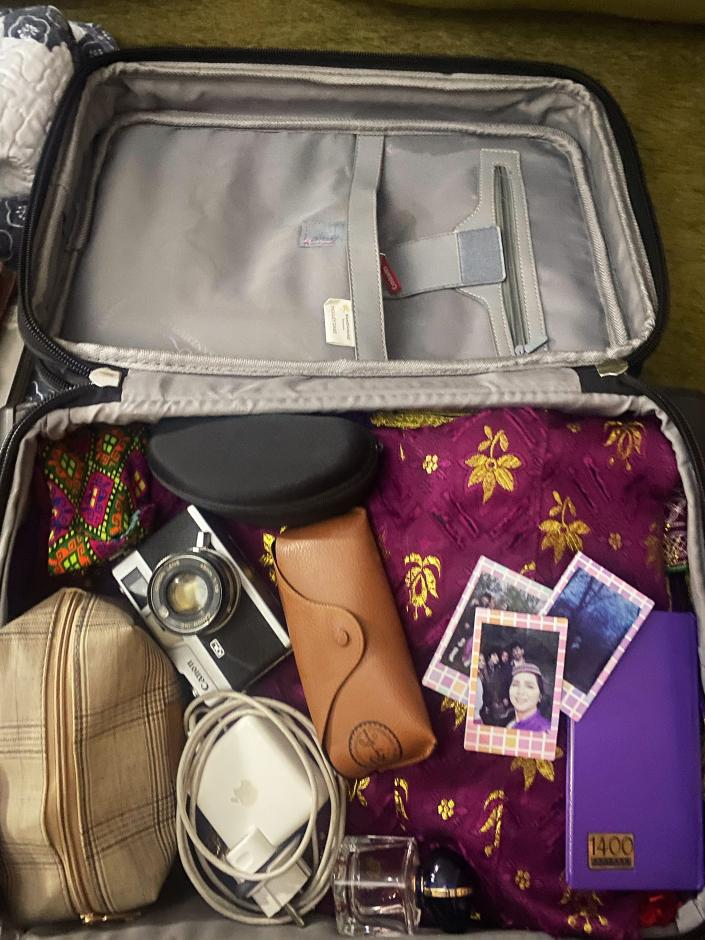 A camera, some fabric, and pictures are seen in a packed suitcase.
