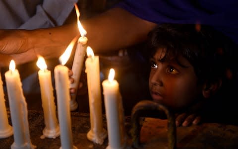 A Pakistani Christian child looks on as adults light candles to pay tribute to Sri Lankan blasts victims - Credit: Rizwan Tabassum/AFP